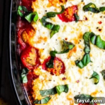 Overhead shot of goat cheese dip in black baking dish, garnished with fresh basil and red pepper flakes, ready to be served with crusty bread.