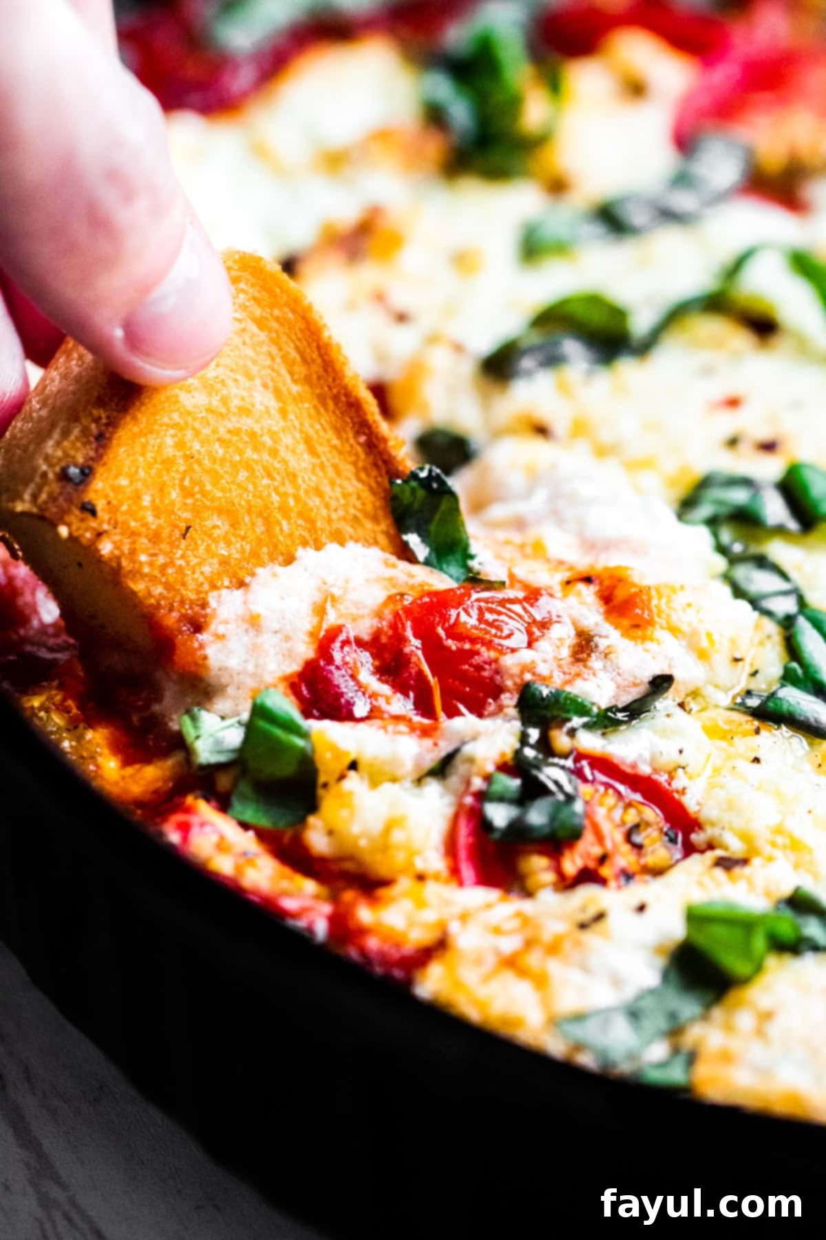 Hand dipping bread into the warm, bubbling baked goat cheese dip, showing the creamy texture.