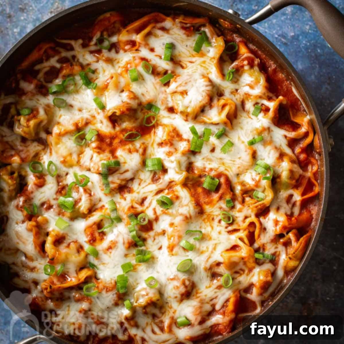 Overhead shot of cheese tortellini in a pot garnished with green onions on a blue speckled surface.