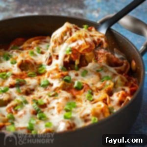 Side close up shot of a fork picking up a piece of cheese tortellini garnished with basil and green onions in a large pot on a blue speckled surface.
