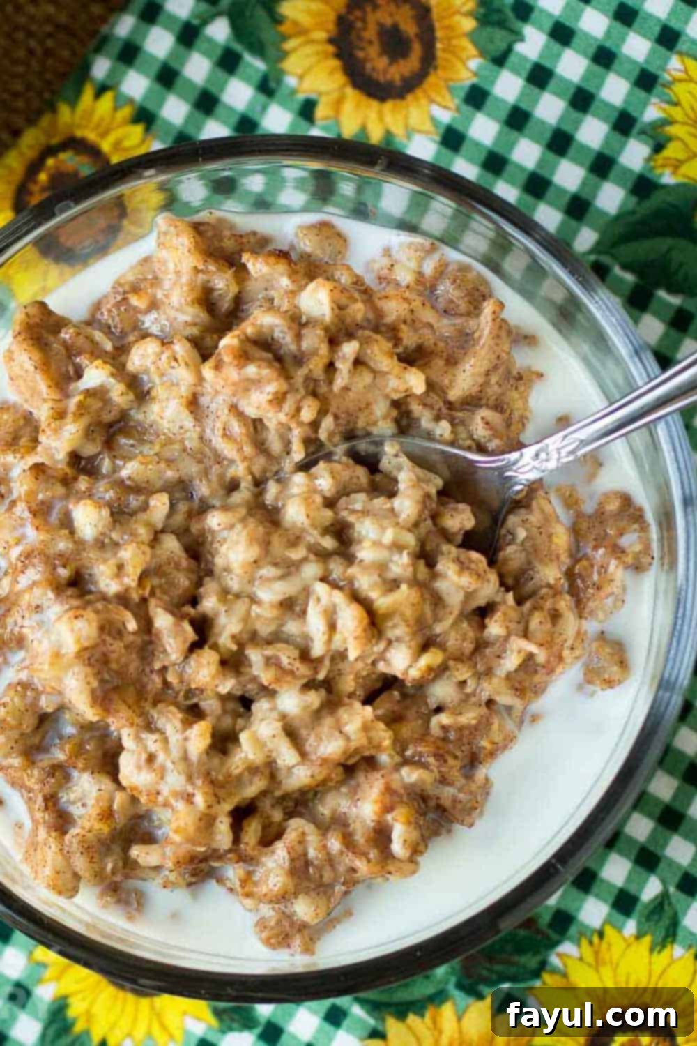 Overhead shot of oatmeal in a clear bowl with a spoon on a green checkered cloth with sunflowers, emphasizing the cozy and delicious nature of the dish.
