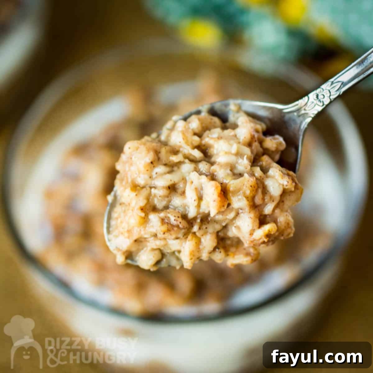 Close up shot of a spoon holding a bite of oatmeal over a clear bowl of oatmeal on a wooden surface, highlighting the inviting texture.