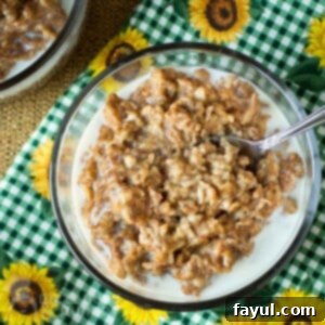 Overhead shot of oatmeal in a clear bowl with a spoon on a green checkered cloth with sunflowers, representing the Slow Cooker Maple Cinnamon Oatmeal.