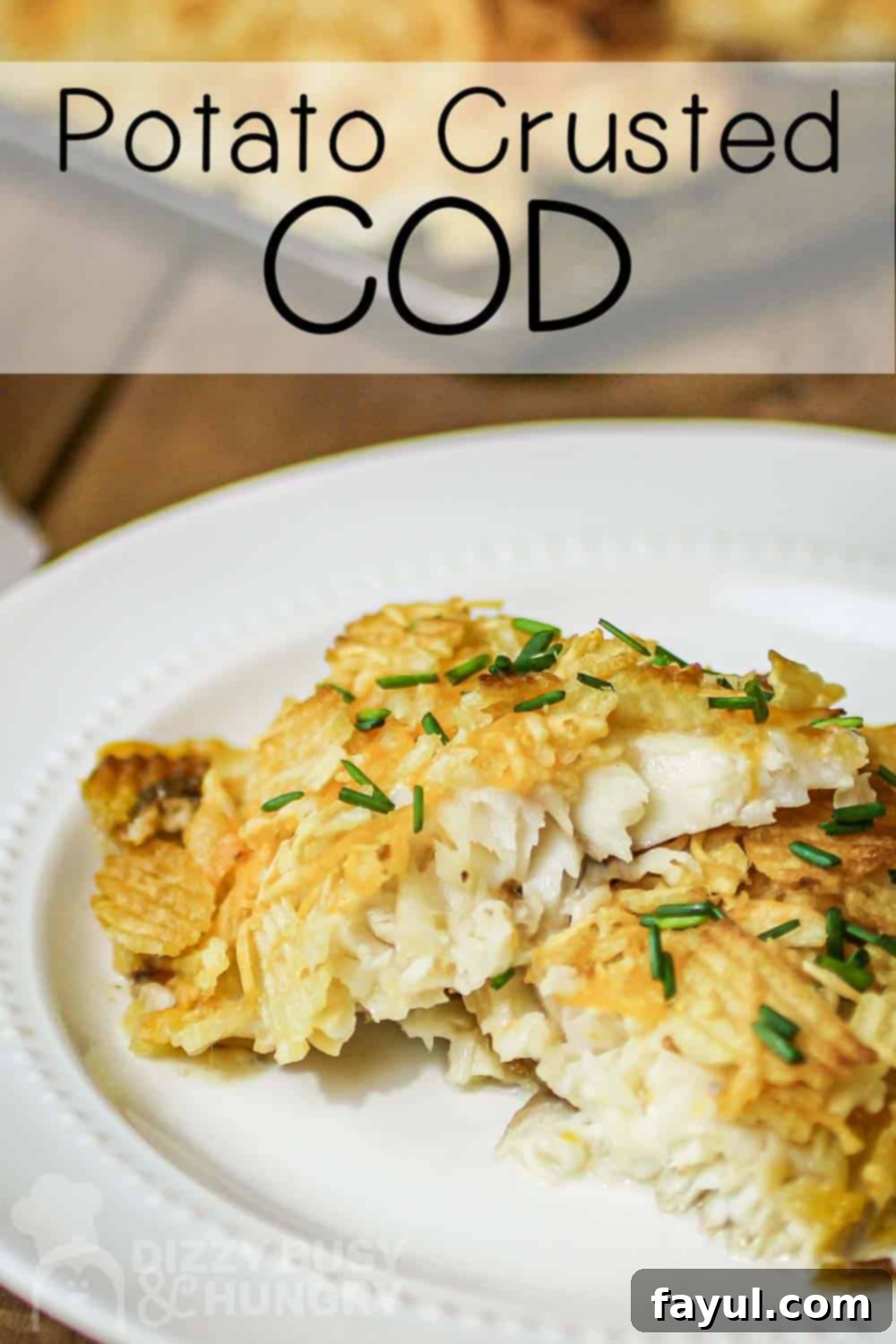 Side view of potato crusted cod on a white plate on a wooden surface with more cod on a baking sheet in the background, showcasing the crispy golden crust.