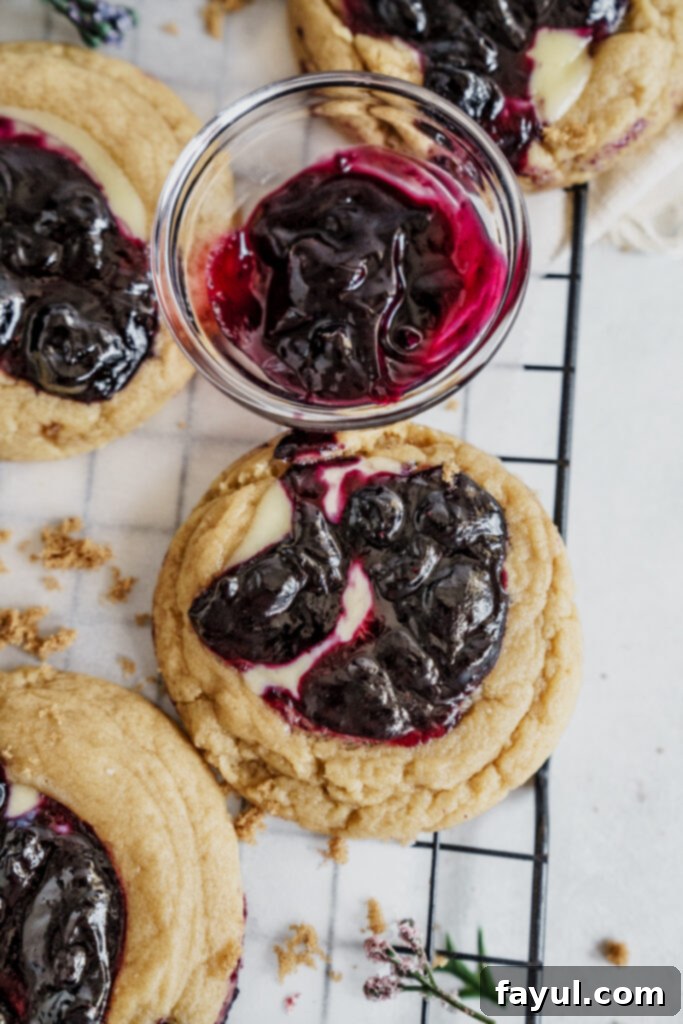 Two blueberry cheesecake cookies arranged on a white surface, showcasing the vibrant filling