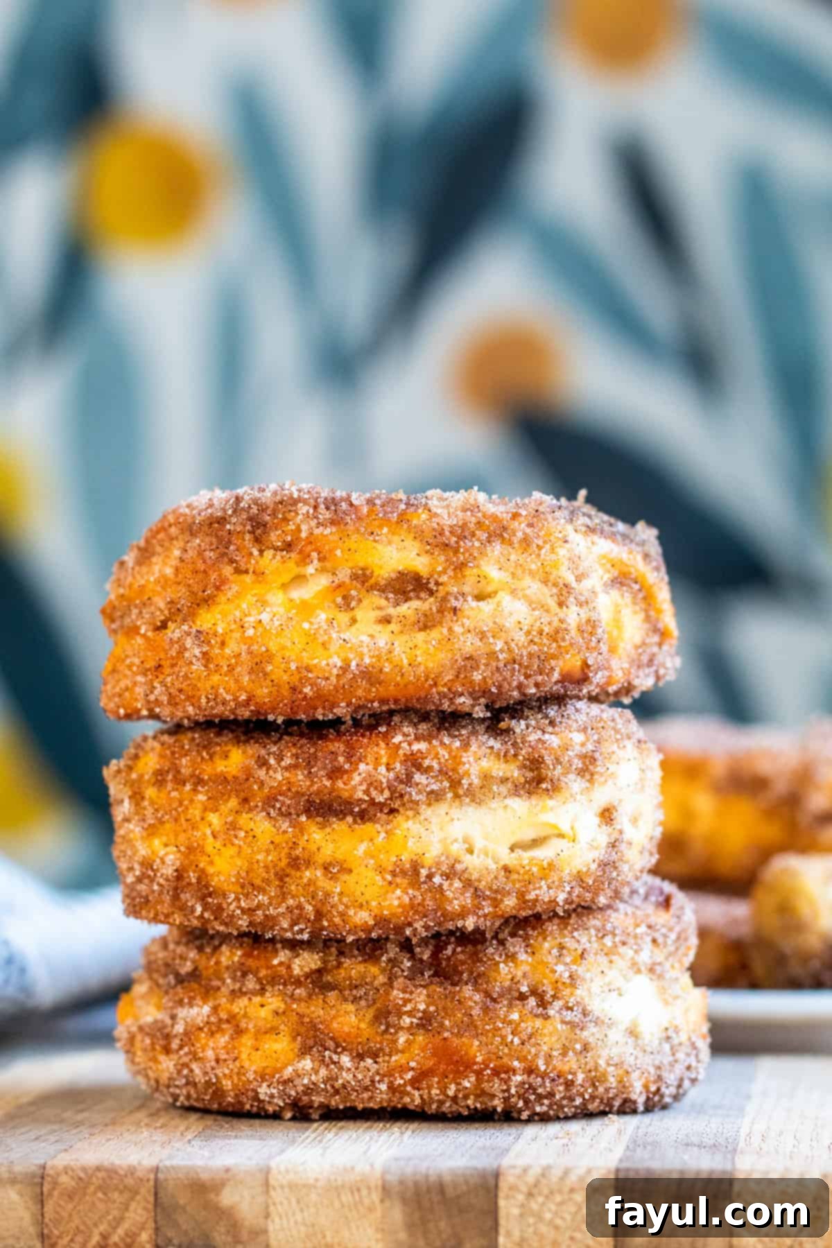 Easy Air Fryer Cinnamon Sugar Biscuit Donuts 2 A stack of golden brown cinnamon sugar air fryer donuts on a plate with a charming blue floral background, inviting you to grab one.