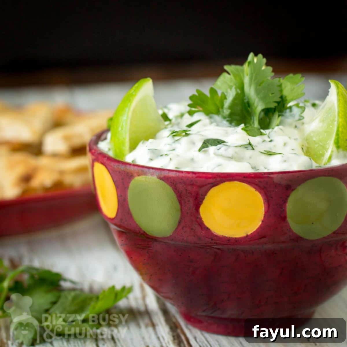 Close up shot of cilantro lime dip garnished with limes and cilantro in a red polka dot bowl with chips in the background.