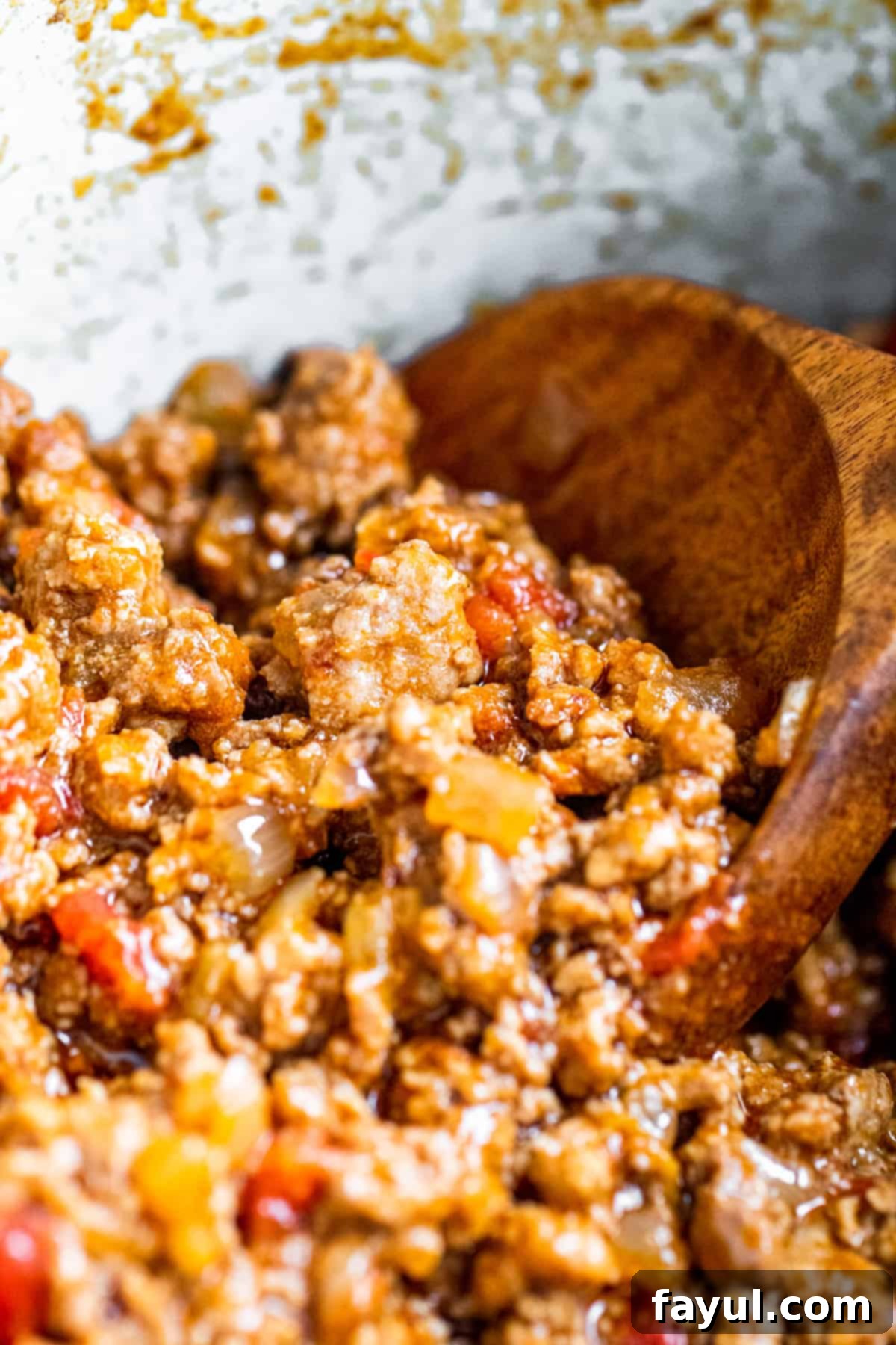 Wooden spoon stirring seasoned taco meat in a white serving bowl.