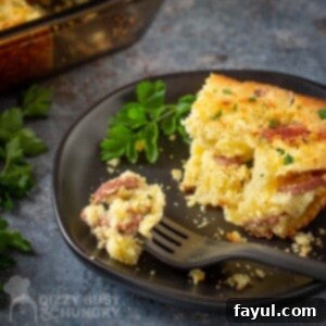 Side shot of a slice of casserole garnished with herbs on a black plate with a black fork holding a piece of casserole on the side.