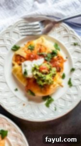 Overhead close-up of a single chicken enchilada puff on a white plate, with decorative fabric and a fork nearby.