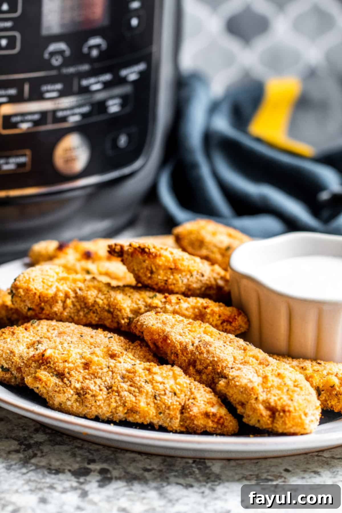 Crispy chicken tenders on a plate with dipping sauce and an air fryer in the background, showcasing a perfect family dinner.