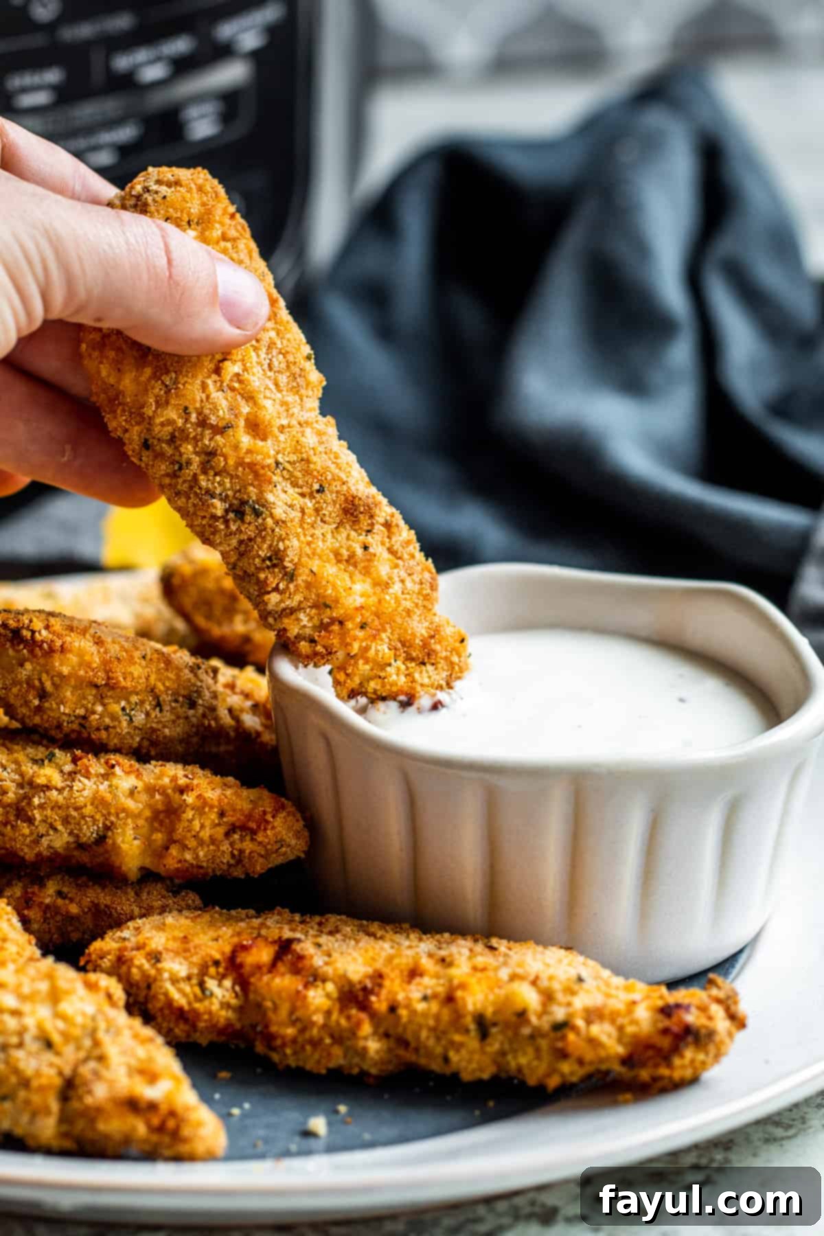 A hand dipping a crispy chicken tender into a white bowl of ranch dressing, emphasizing the delicious pairing.