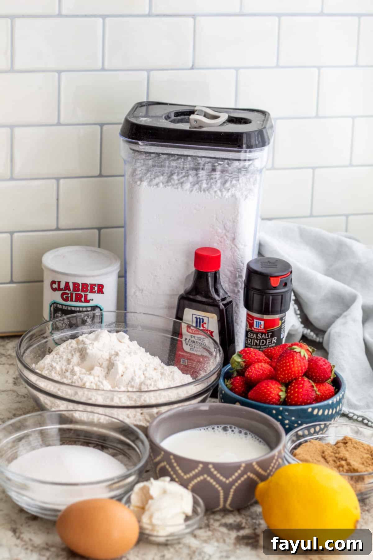 Sunshine Strawberry Lemon Loaf 3 Various ingredients for strawberry loaf cake, including fresh strawberries, flour, sugar, milk, and eggs, neatly laid out on a clean white countertop, ready for baking.