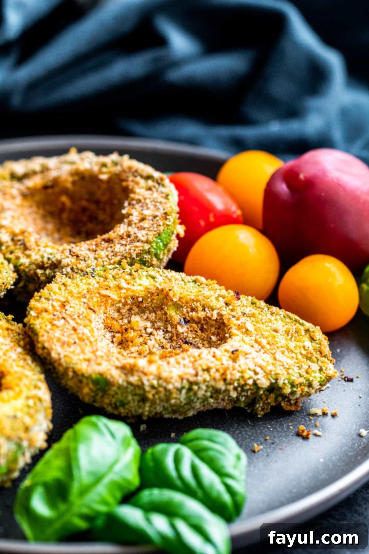 Speedy and Simple Air Fryer Avocados 2 Angle shot of fried avocados on a gray plate with tomatoes and basil.