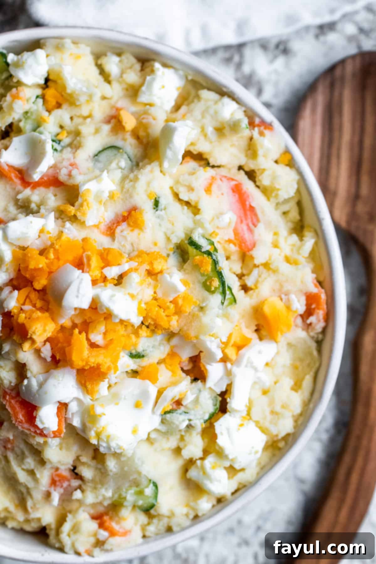 Overhead shot of Japanese potato salad in white bowl on counter, garnished with fresh herbs and sliced eggs.
