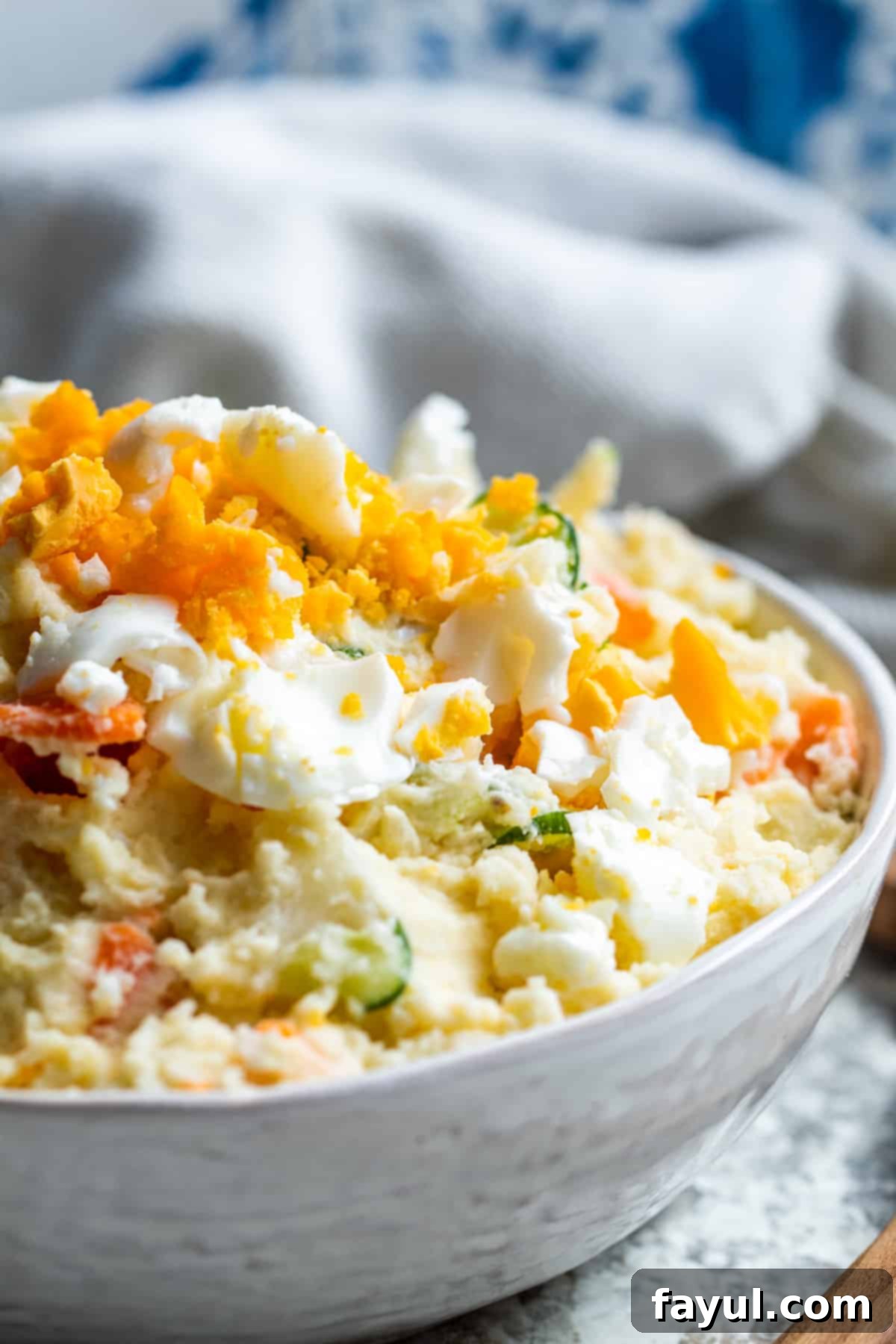 Close up angle of creamy Japanese potato salad in a white bowl, showing mashed potatoes, vegetables, and egg.
