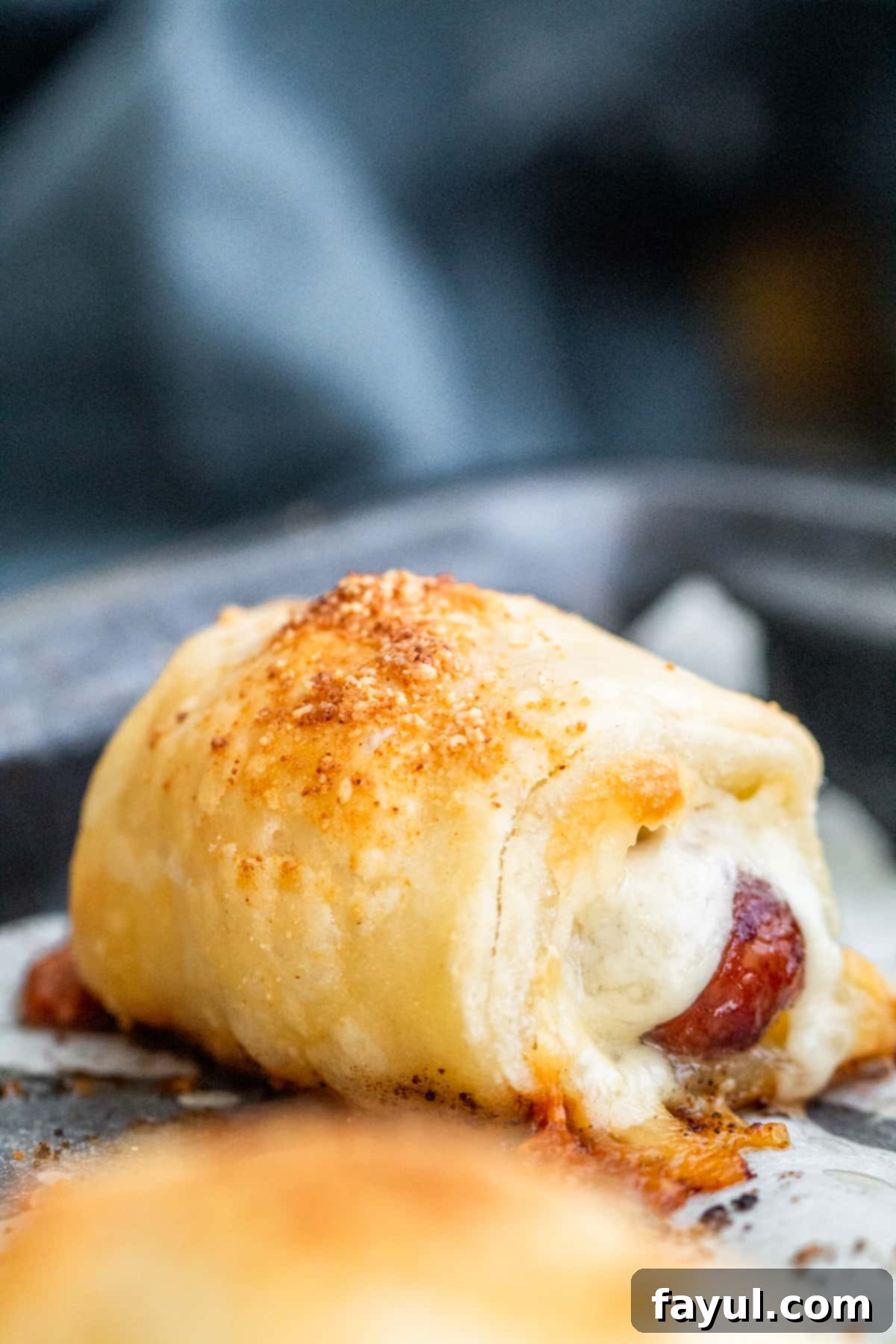 Flaky Cheesy Pigs in a Blanket 2 Close up shot of golden brown, cheesy pigs in a blanket on parchment paper, fresh from the oven, showing the flaky puff pastry and melted cheese peeking out.