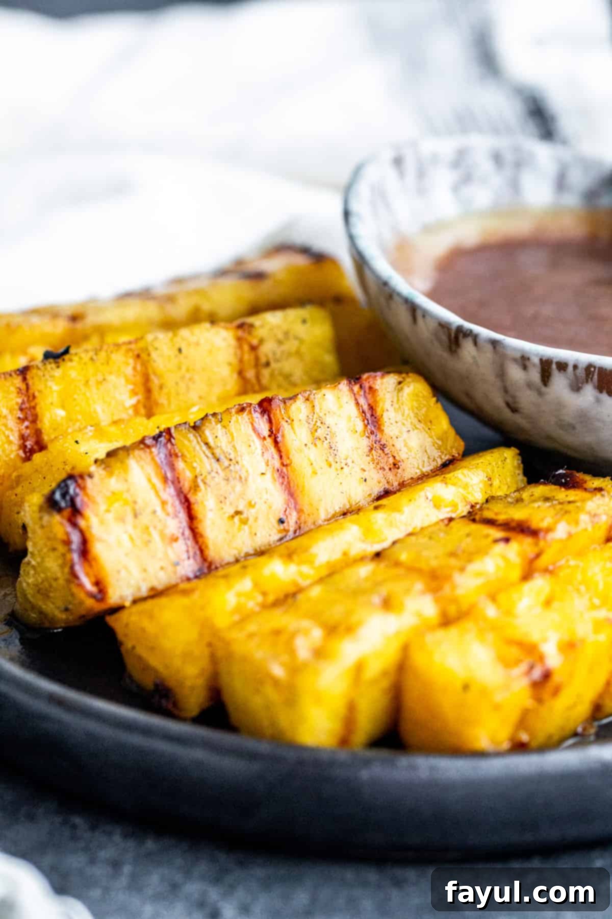 Cinnamon Kissed Grilled Pineapple 2 Strait on shot of pineapple on a plate with sauce.