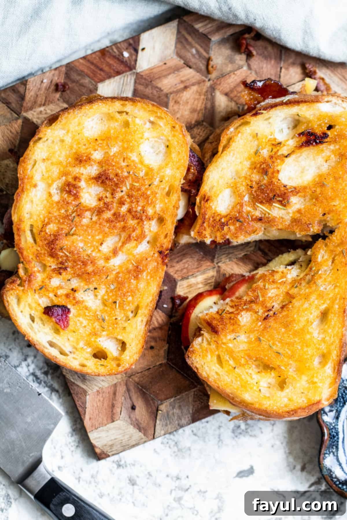 Overhead shot of two sandwiches, one cut in half, on wooden cutting board.