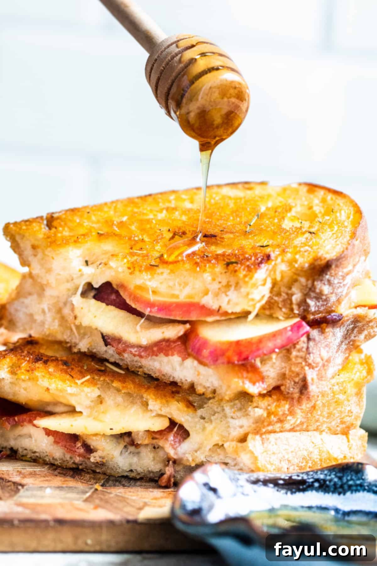 Hand drizzling honey over top of stack of sandwiches.