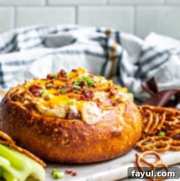 Baked dip in a bread bowl on white counter sitting on serving tray.