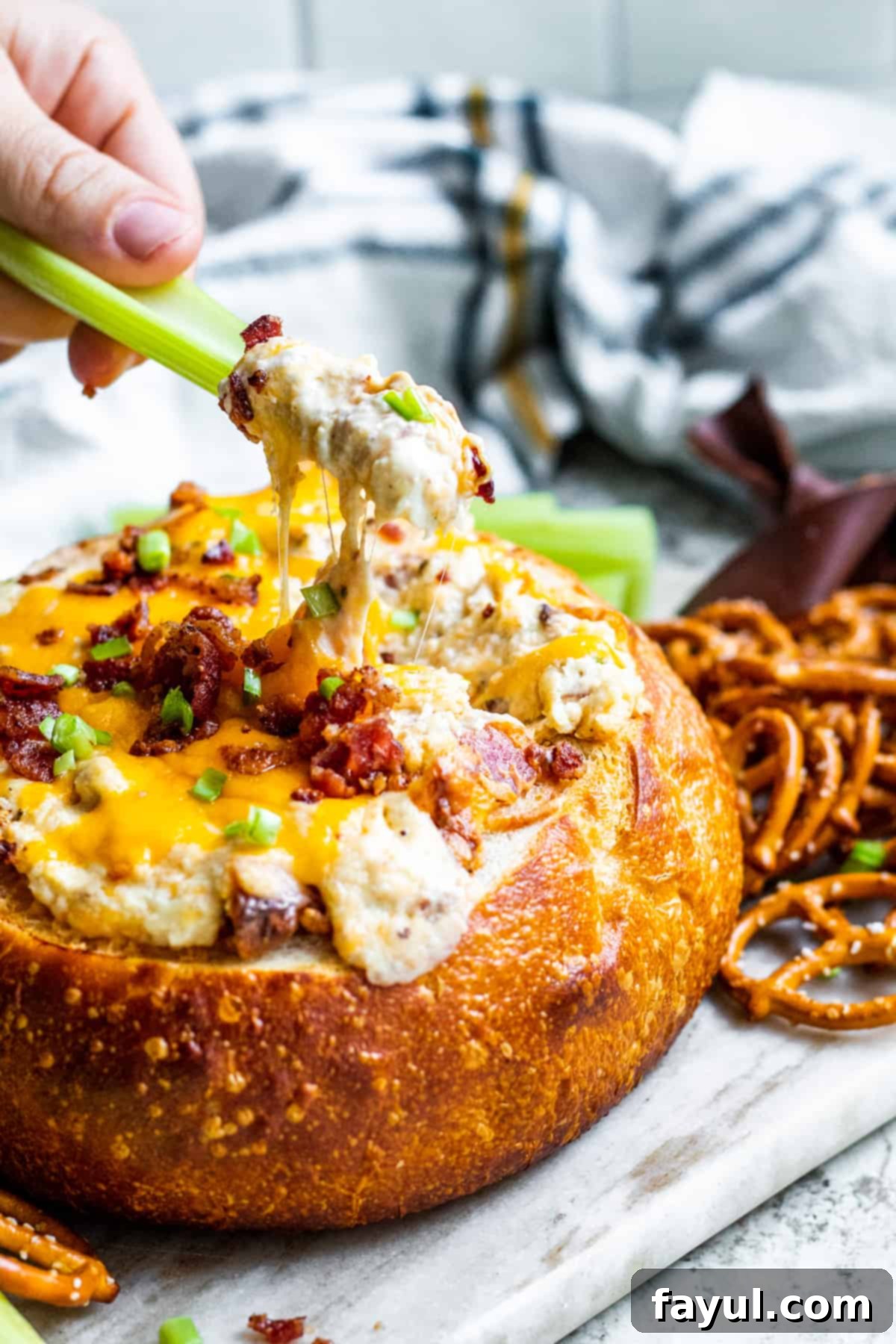 Smoky Bacon Cheese Bread Bowl Fondue 6 Celery being dipped into the warm bacon cheese dip in a sourdough bread bowl.