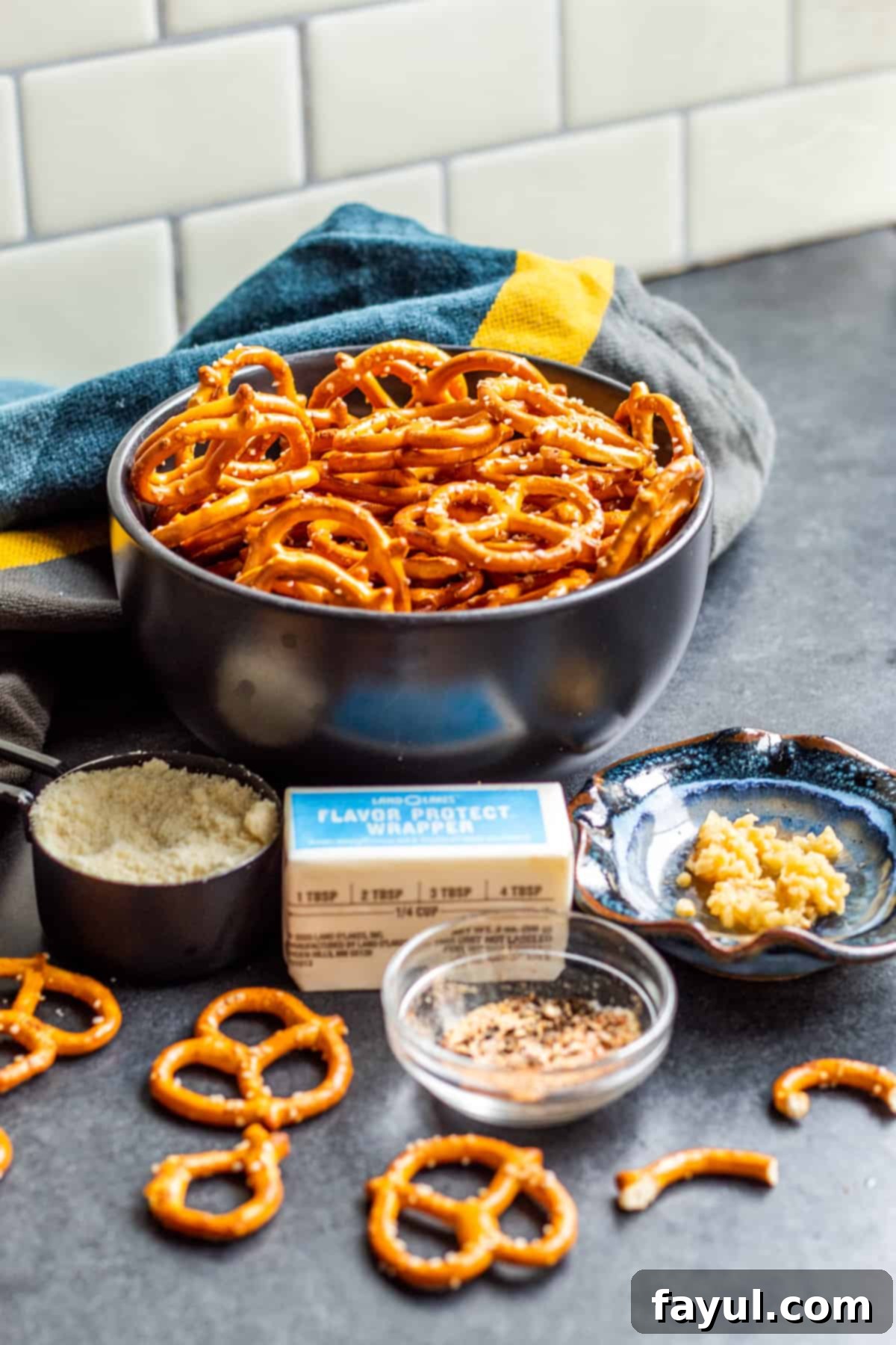 Simple Garlic Parmesan Pretzels 3 All the ingredients for making garlic parmesan pretzels laid out on a dark wooden table in small white bowls, including pretzels, butter, garlic, and cheese.