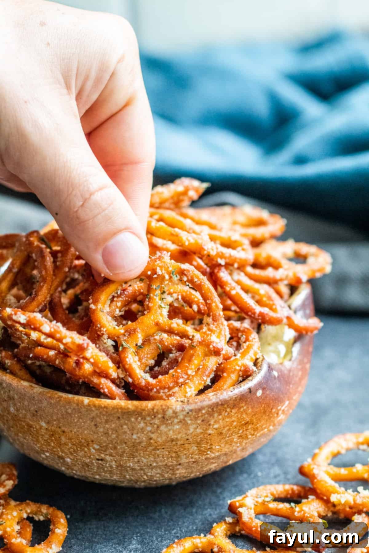 Simple Garlic Parmesan Pretzels 6 A hand reaches into a brown bowl of garlic parmesan pretzels to pick one up.