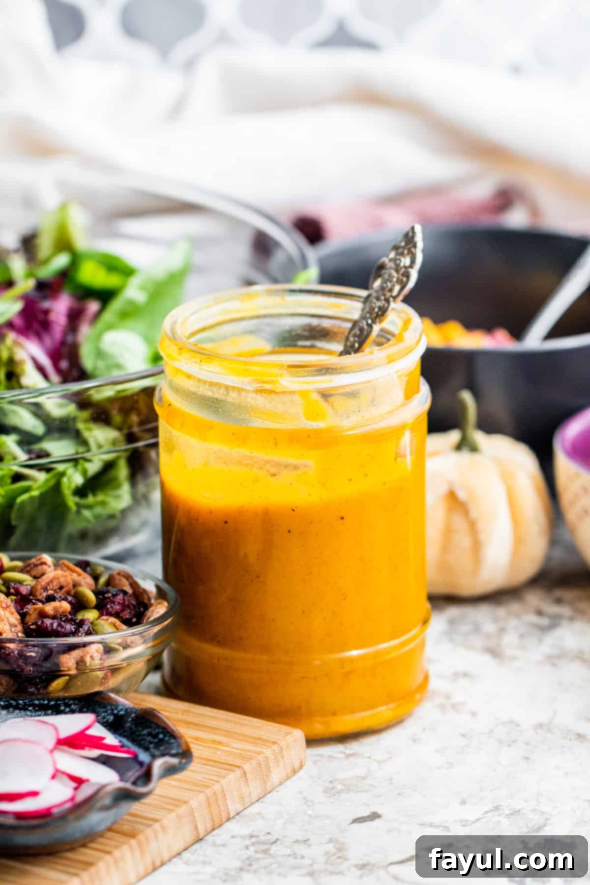 Golden Maple Pumpkin Dressing 32 Dressing in a glass jar with salad ingredients like lettuce, cherry tomatoes, and pumpkin around it.