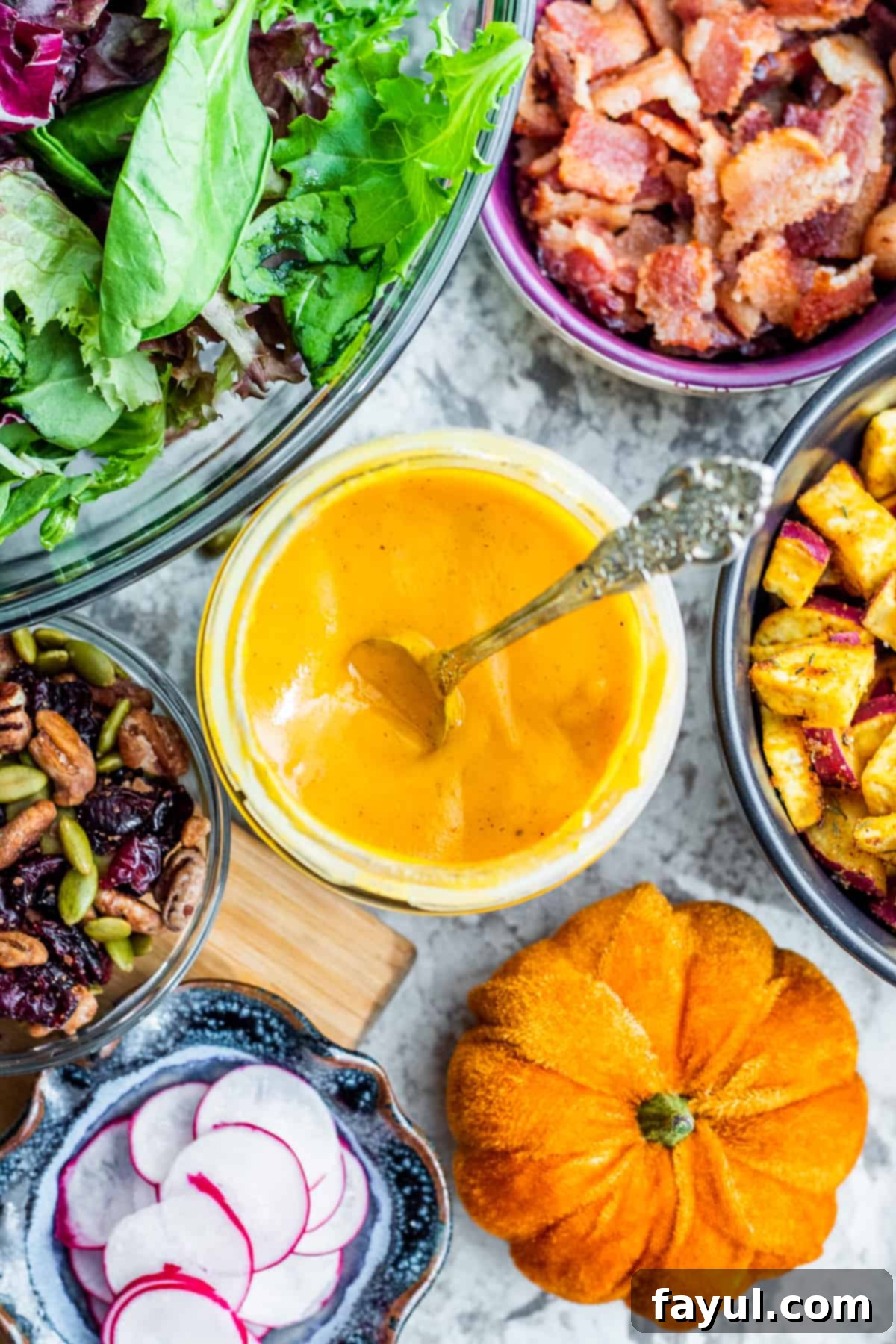 Overhead shot of pumpkin salad dressing in jar with silver spoon in it with salad ingredients.