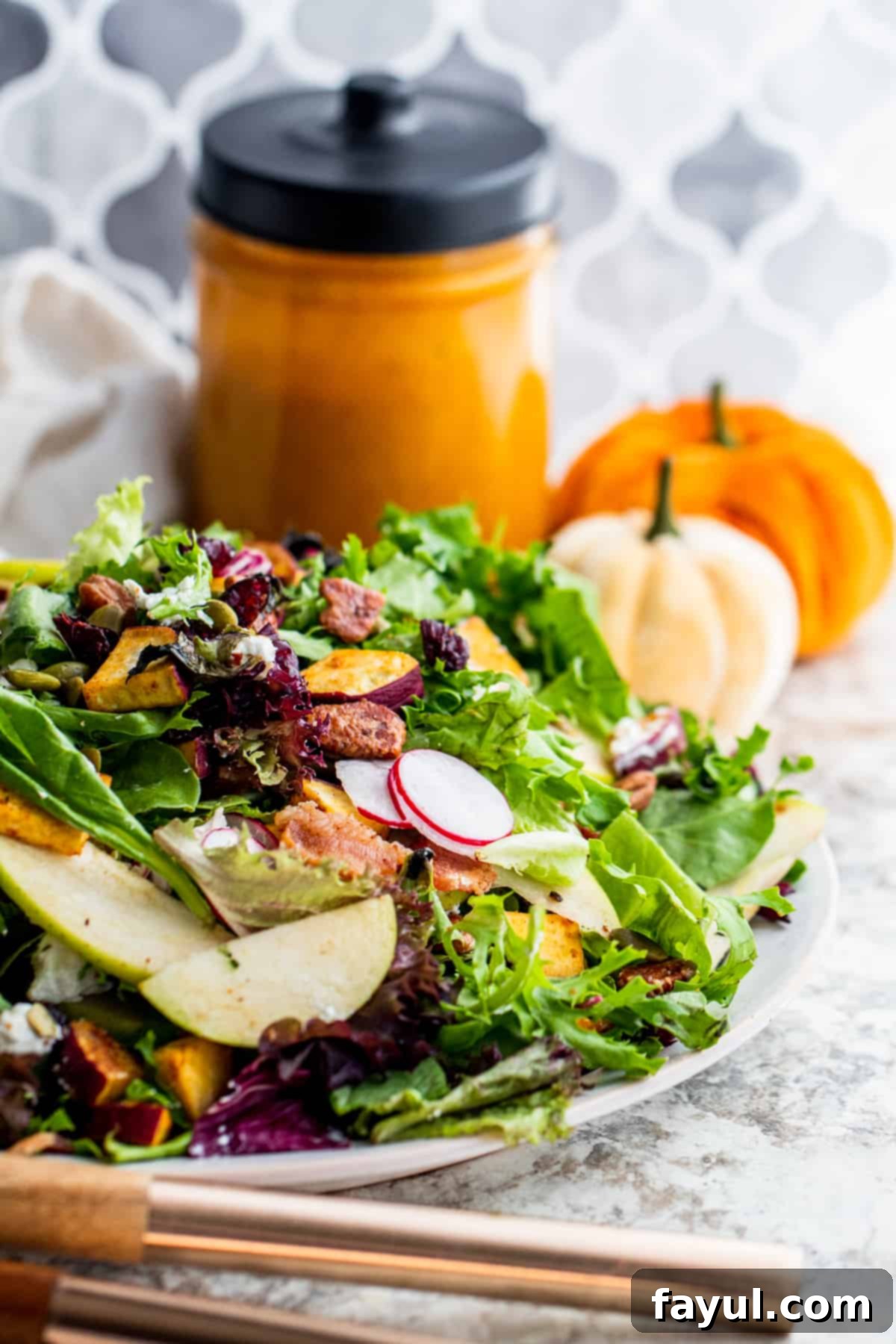 A generously portioned Fall Harvest Salad on a large white plate, drizzled with a rich dressing, with a rustic pumpkin and autumn decor in the softly blurred background.