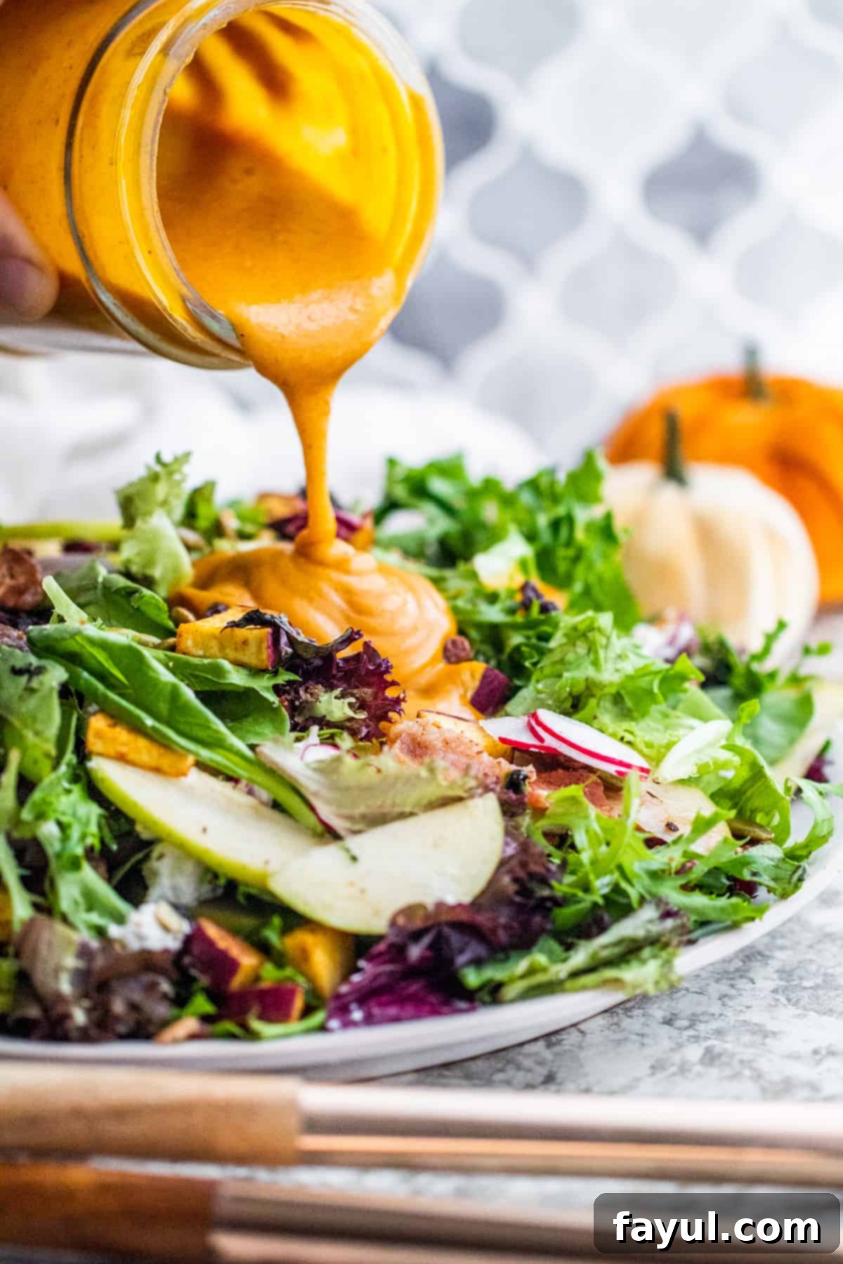 A close-up shot of a hand elegantly pouring golden maple pumpkin dressing over a vibrant bowl of fresh greens, showcasing the delicious moment just before the salad is tossed and served.