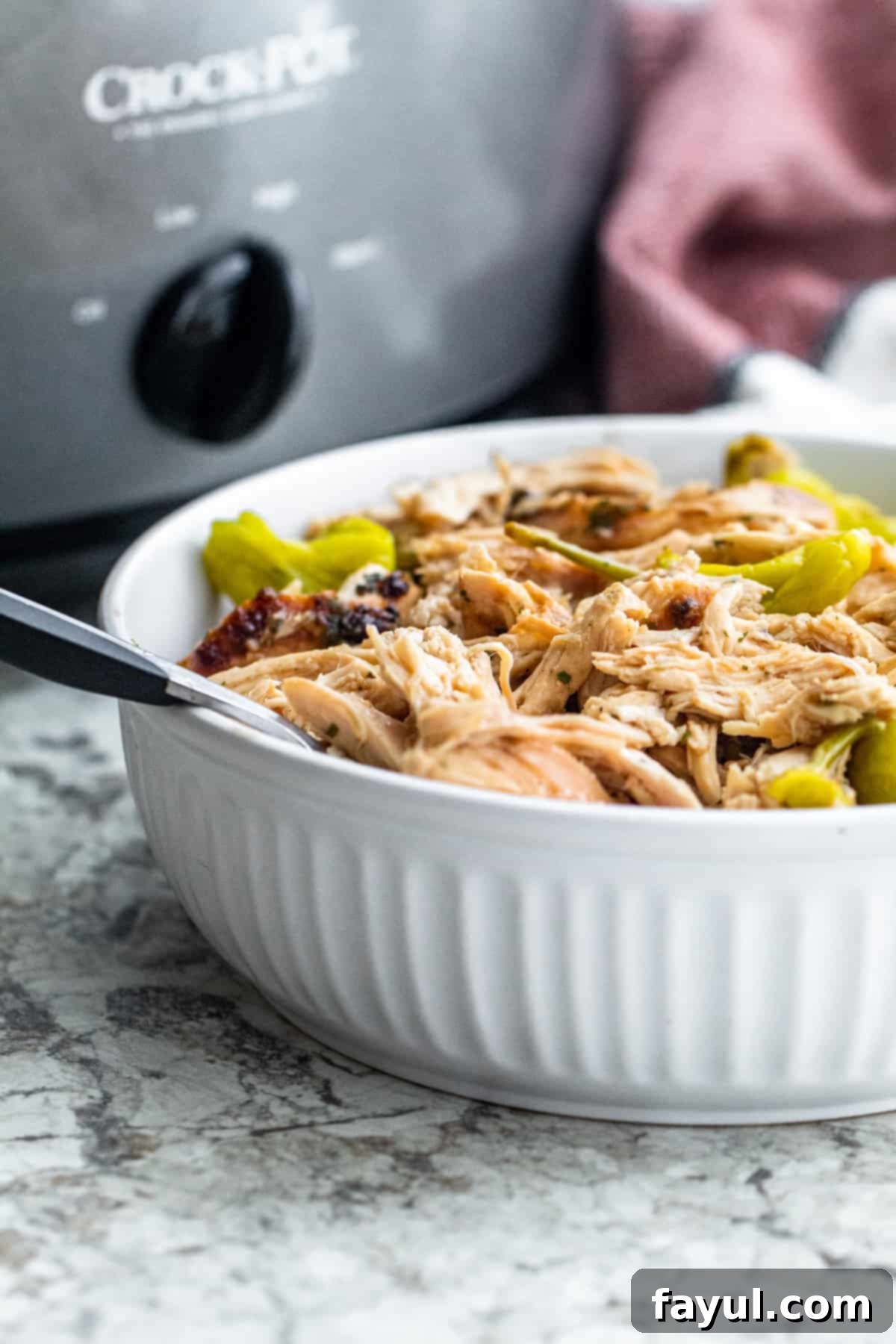 Mississippi shredded chicken in a large white bowl with a fork in it, ready to be served.