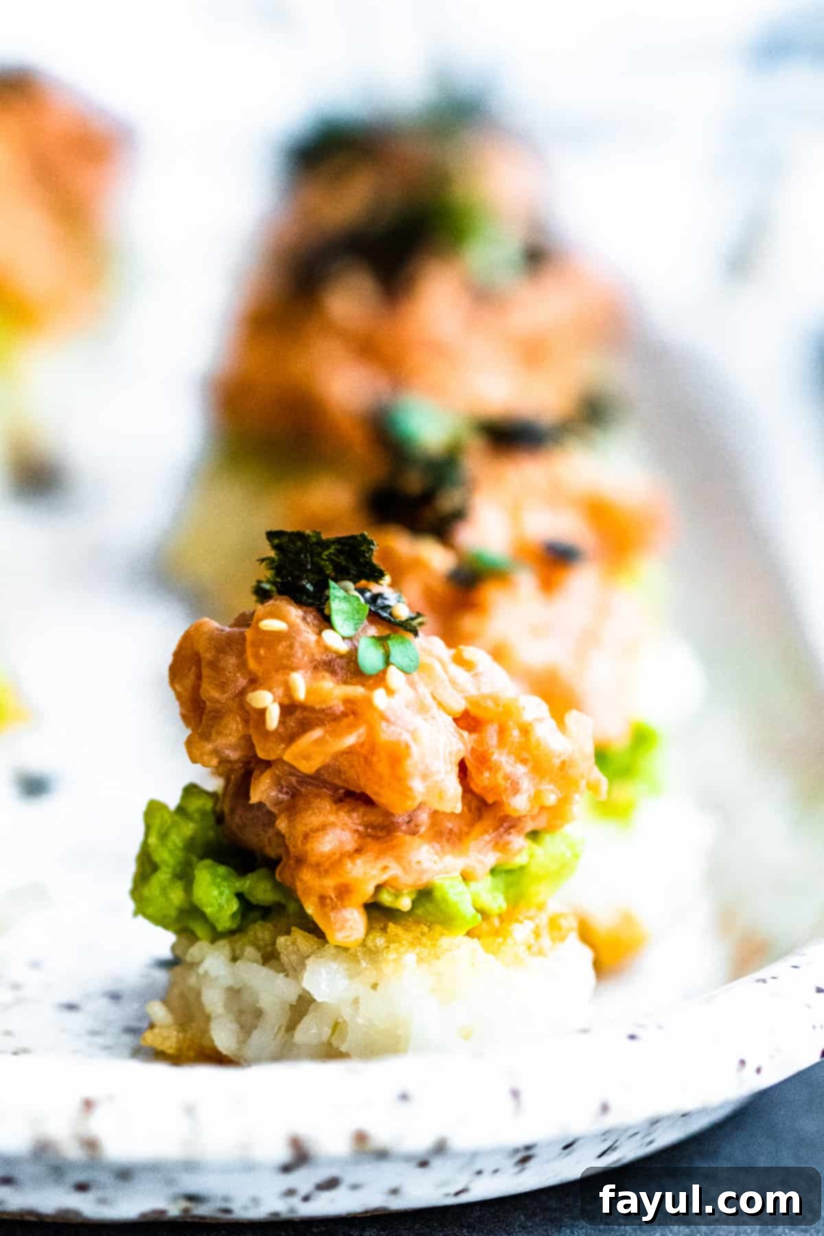 Freshly prepared Spicy Tuna Crispy Rice Sushi rolls arranged neatly in a line on a platter, garnished with sesame seeds.