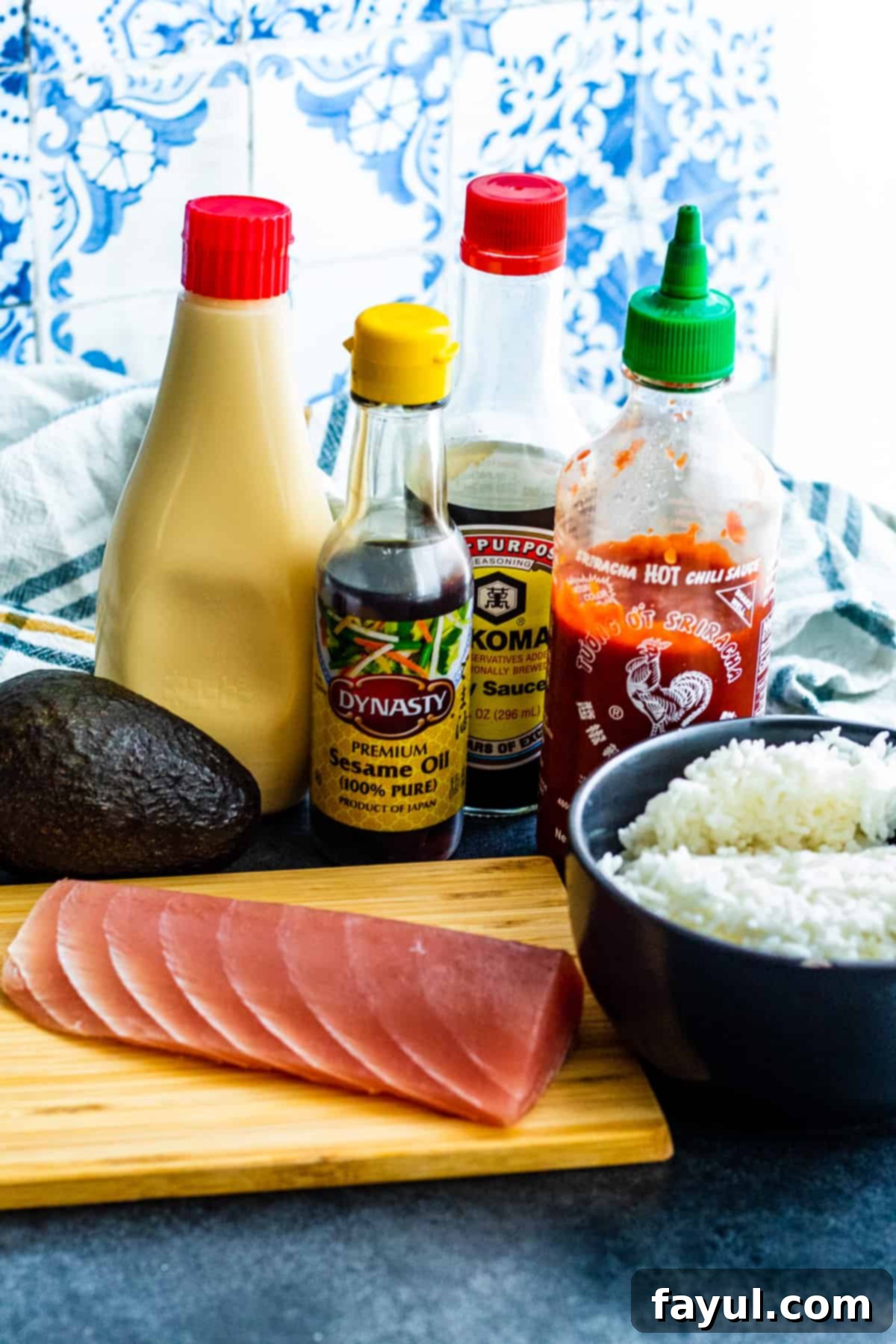 Various fresh ingredients for Spicy Tuna Crispy Sushi laid out attractively in small bowls and on a wooden cutting board on a blue kitchen counter.