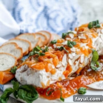 A close-up of the beautifully textured Honey Apricot Goat Cheese Log on a white marble tray, with an inviting scattering of crackers around it.