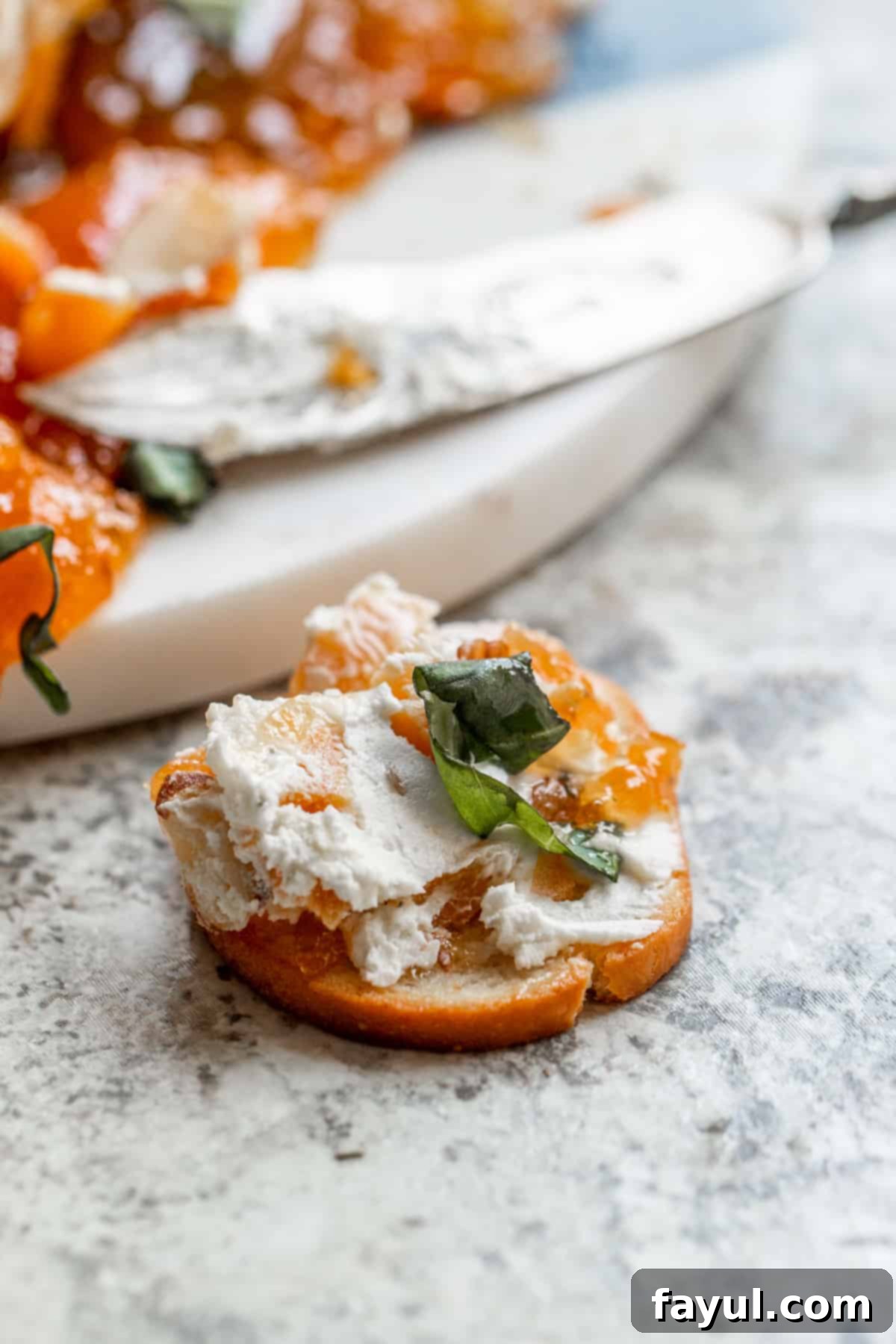 A close-up shot of the creamy goat cheese log spread onto a cracker, garnished with a tiny piece of fresh basil.