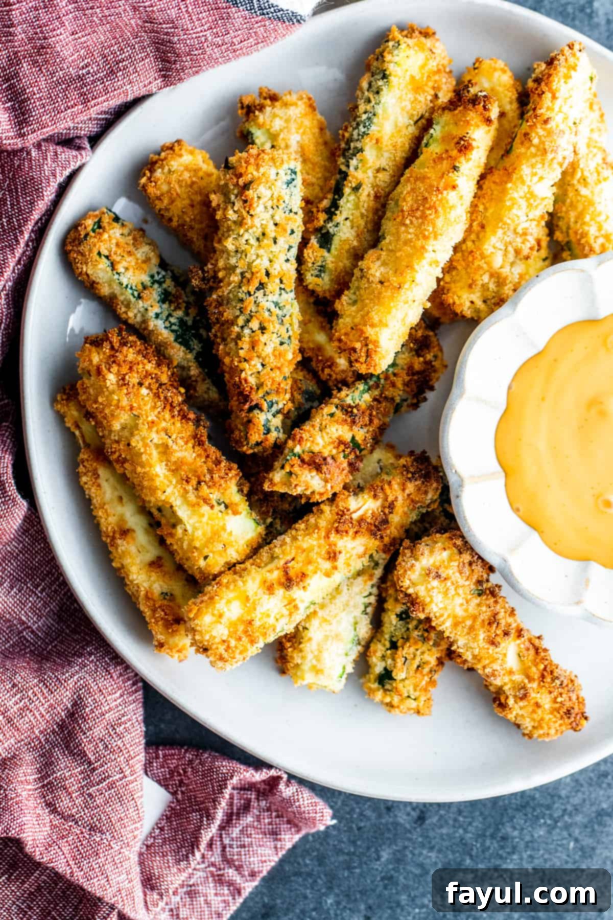 Crispy Garlic Parmesan Air Fryer Zucchini Fries 32 Overhead shot of golden brown, crispy air-fried zucchini fries on a white plate with a small bowl of dipping sauce.
