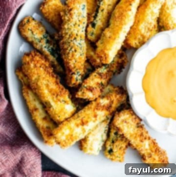 Crispy Garlic Parmesan Air Fryer Zucchini Fries 11 Overhead shot of golden brown, crispy air-fried zucchini fries on a white plate with a small bowl of dipping sauce.
