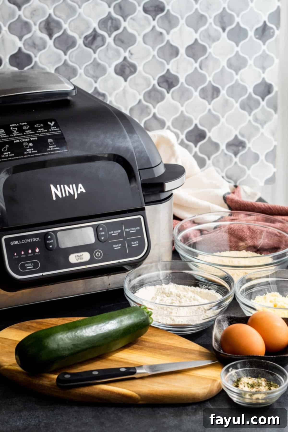 Crispy Garlic Parmesan Air Fryer Zucchini Fries 3 Ingredients for garlic parmesan zucchini fries laid out in individual glass bowls on a dark blue counter, including zucchini, flour, breadcrumbs, and spices.