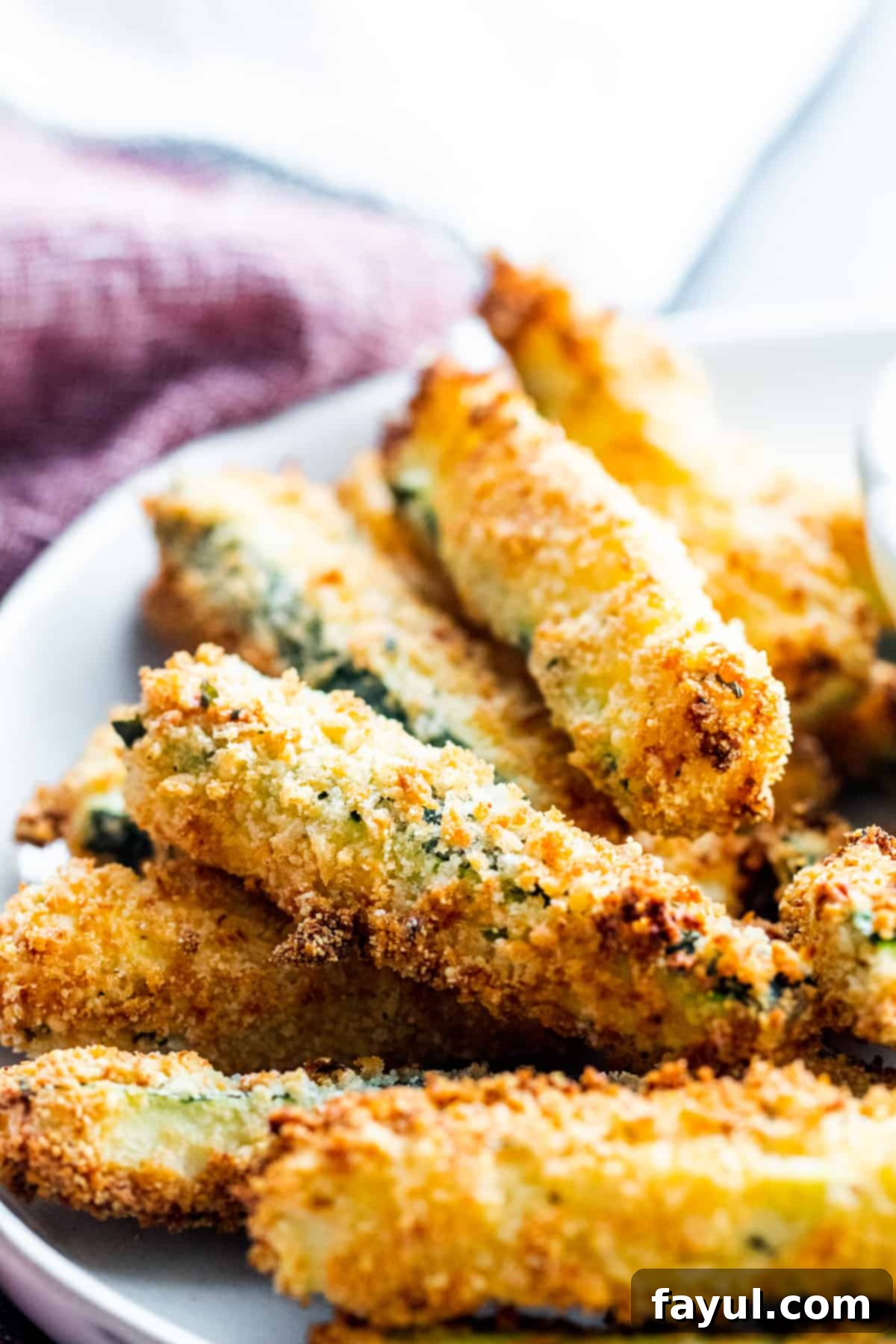 Crispy Garlic Parmesan Air Fryer Zucchini Fries 7 Close up shot of a pile of golden crispy garlic parmesan zucchini fries on a white plate, perfectly cooked and ready to be served.