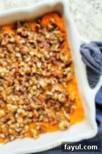 The best Southern Sweet Potato Casserole perfect for family holidays like Thanksgiving, Christmas and Easter! This easy holiday side dish is ready in about 40 minutes and can be made ahead of time for easy morning prep. This traditional southern dish has been a family favorite and tradition for over 70 years! Step by step recipe instructions, images, and VIDEO included! #recipe #food #Thanksgiving #casserole #holidays #familytradition #easyrecipe #vegetarian Overhead shot of a golden-brown Southern Sweet Potato Casserole with a crunchy pecan topping in a white baking dish, set on a bright white counter, ready for a holiday feast.