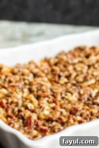 The best Southern Sweet Potato Casserole perfect for family holidays like Thanksgiving, Christmas and Easter! This easy holiday side dish is ready in about 40 minutes and can be made ahead of time for easy morning prep. This traditional southern dish has been a family favorite and tradition for over 70 years! Step by step recipe instructions, images, and VIDEO included! #recipe #food #Thanksgiving #casserole #holidays #familytradition #easyrecipe #vegetarian A beautifully baked Southern Sweet Potato Casserole in a white baking dish on a white counter, showcasing the golden pecan topping, ready to be served at a holiday meal.