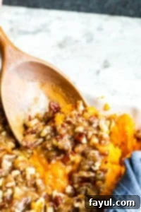 The best Southern Sweet Potato Casserole perfect for family holidays like Thanksgiving, Christmas and Easter! This easy holiday side dish is ready in about 40 minutes and can be made ahead of time for easy morning prep. This traditional southern dish has been a family favorite and tradition for over 70 years! Step by step recipe instructions, images, and VIDEO included! #recipe #food #Thanksgiving #casserole #holidays #familytradition #easyrecipe #vegetarian A wooden spoon scooping out a generous portion of creamy Southern Sweet Potato Casserole with a crispy pecan topping from a white baking dish, highlighting its delicious texture.