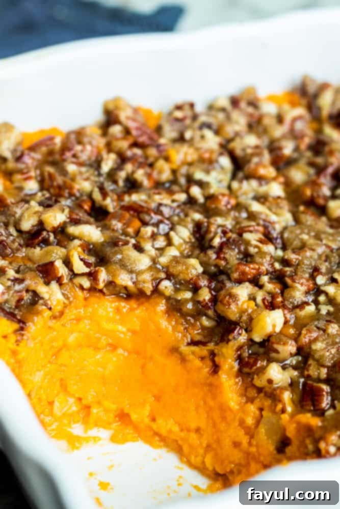 Southern Pecan-Crusted Sweet Potato Delight 2 A generous scoop of Southern Sweet Potato Casserole with its golden pecan topping, served fresh out of a white baking dish, indicating its rich and comforting texture.