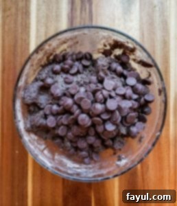 Dark chocolate chips being folded into the thick chocolate cookie dough.