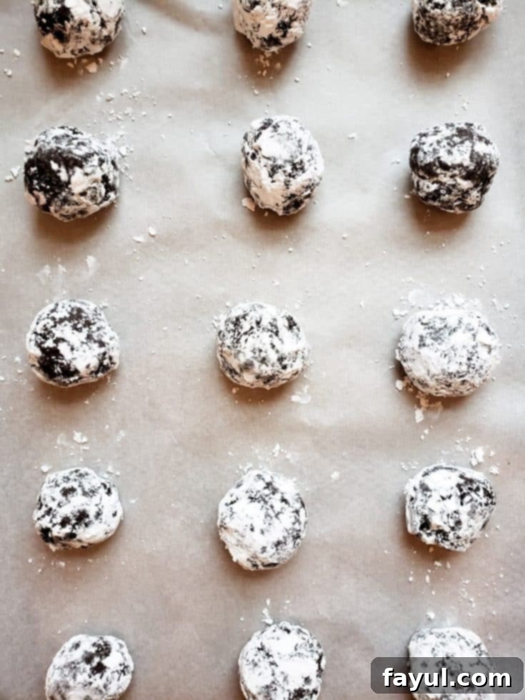 Overhead shot of chocolate cake cookie dough balls coated in powdered sugar on parchment paper, ready for baking.