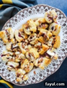 Overhead shot of freshly baked blackberry puff pastry bites arranged on a white plate with elegant flower trim, set on a rustic blue kitchen counter.