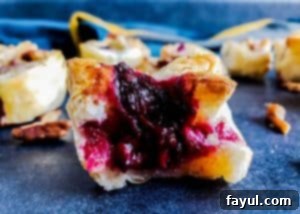 A close-up image of a single Blackberry Brie Bite with Pecan Sage topping, perfectly baked and sitting on a blue countertop, with other blurred bites in the background.