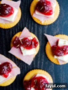 Close-up of several Ritz Bites with Ham, Brie, and Cranberries arranged on a black surface, viewed from above.